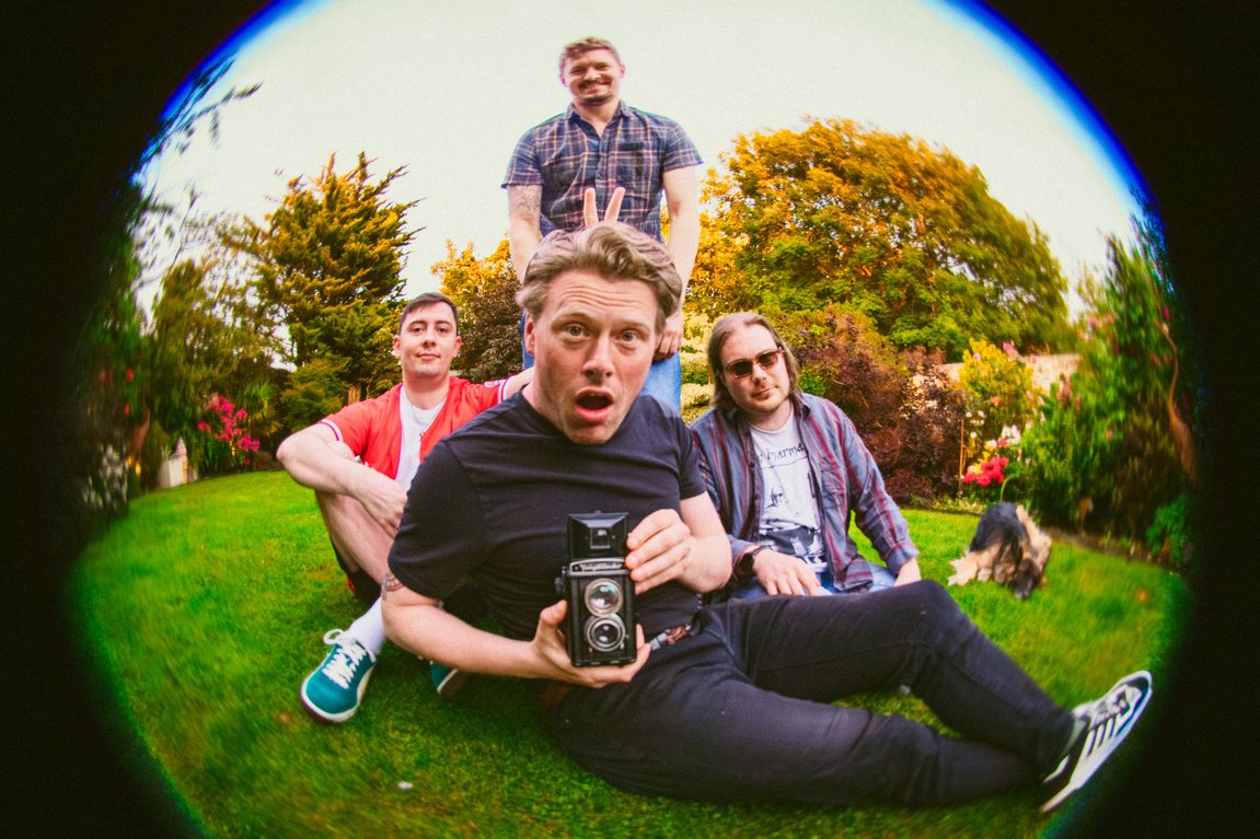 The four members of Monite sprawled on a garden lawn, shot on a fisheye lens